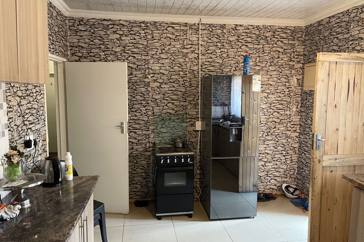 A functional kitchen featuring granite countertops, built-in cabinetry, and a freestanding stove, with tiled flooring and a timber ceiling.