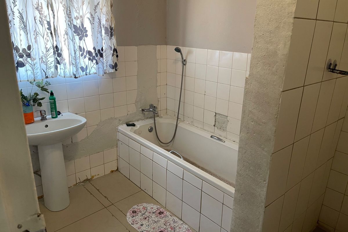 A dated bathroom featuring a pedestal basin and a built-in bathtub, currently requiring significant repairs to wall tiling and plaster finishes.