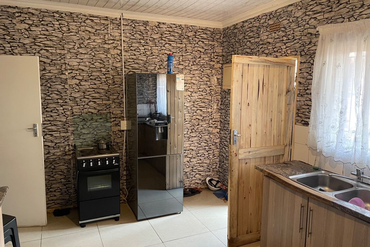 A functional kitchen featuring tiled flooring, laminate cabinetry, a double bowl sink, and a freestanding stove, with potential for cosmetic modernization.