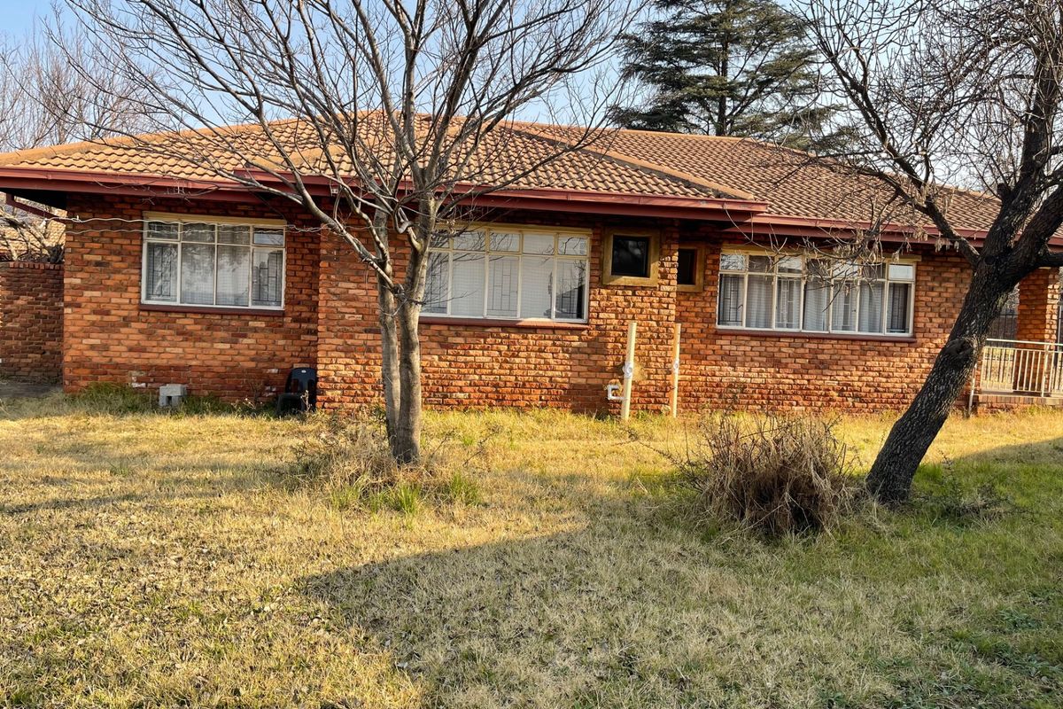 Rear view of a single-story face brick house featuring a tiled roof and security-fitted windows, set within a large garden area.