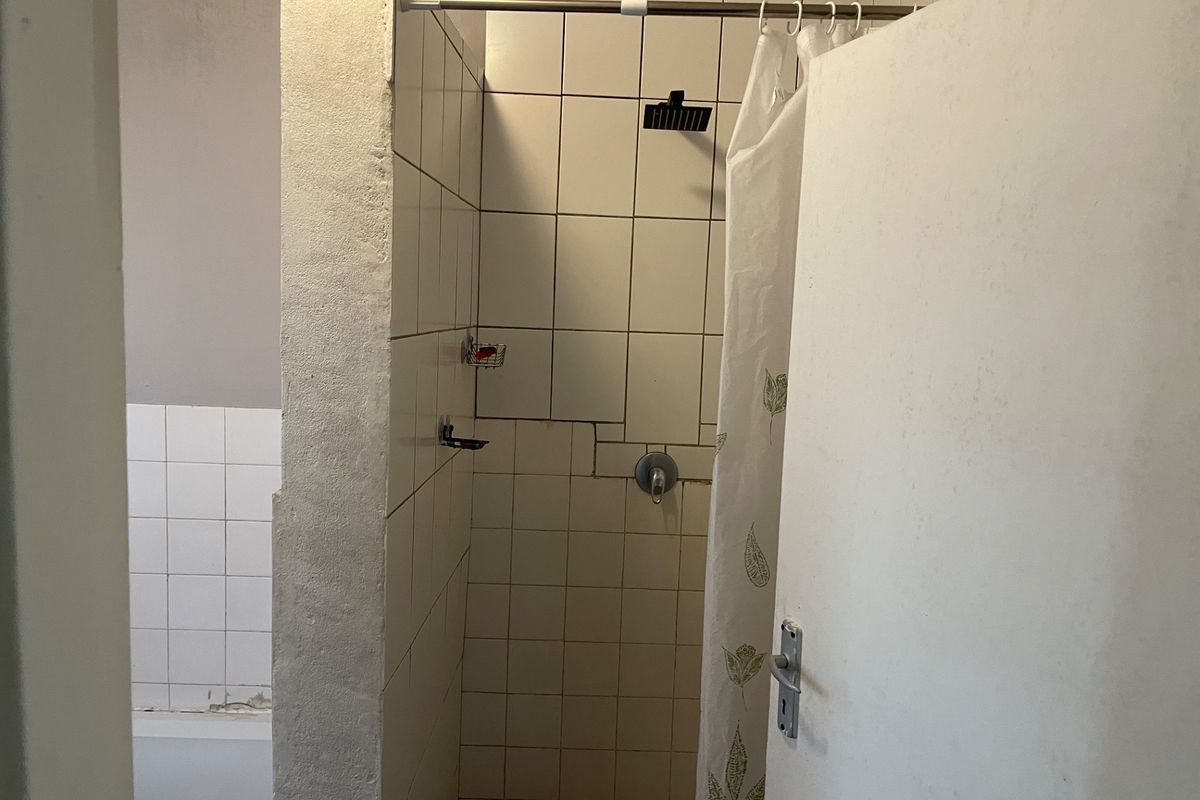 A functional bathroom shower area featuring tiled walls and a modern shower head, currently requiring cosmetic updates to the tile work and finishes.