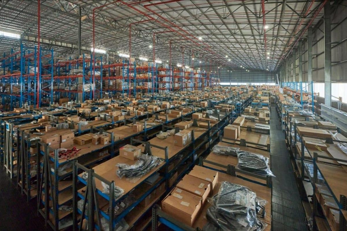 Large-scale commercial warehouse facility featuring extensive industrial steel racking systems, high-bay lighting, and an exposed steel truss roof structure.