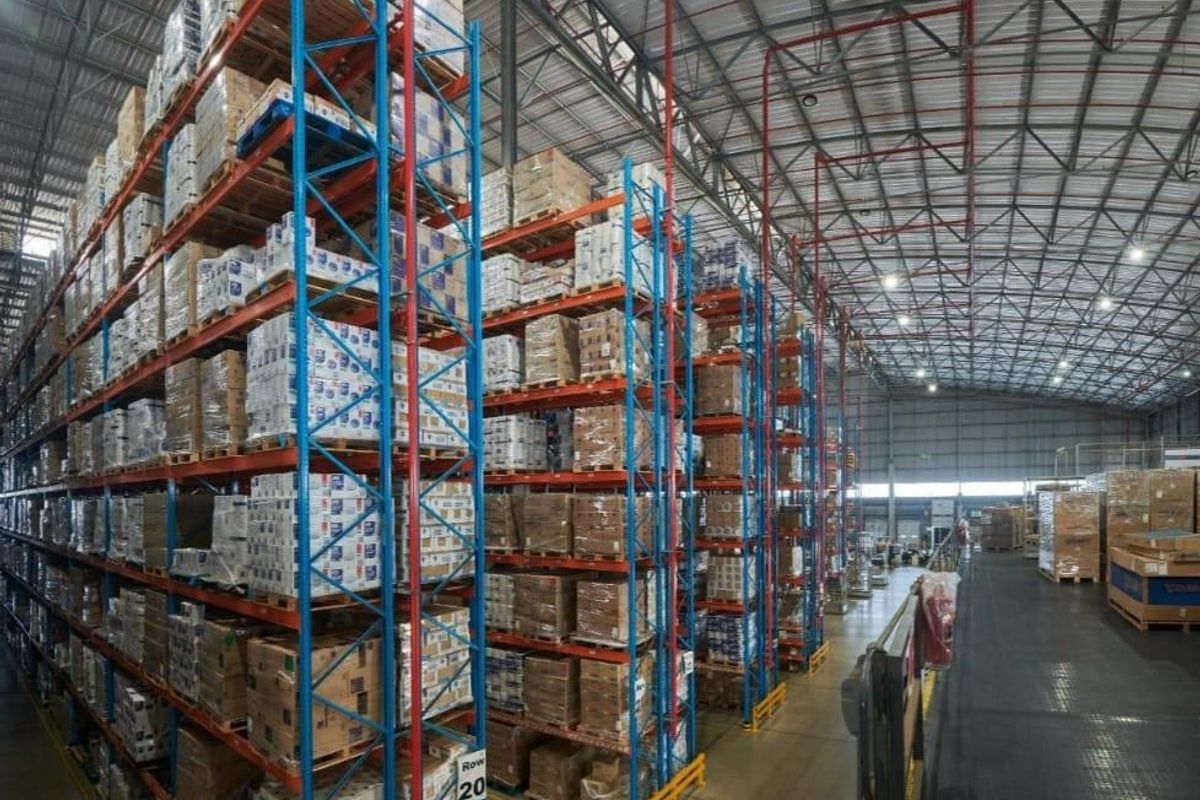 Large commercial warehouse space featuring high-bay industrial racking systems, exposed steel roof trusses, and durable concrete flooring with integrated fire sprinkler infrastructure.