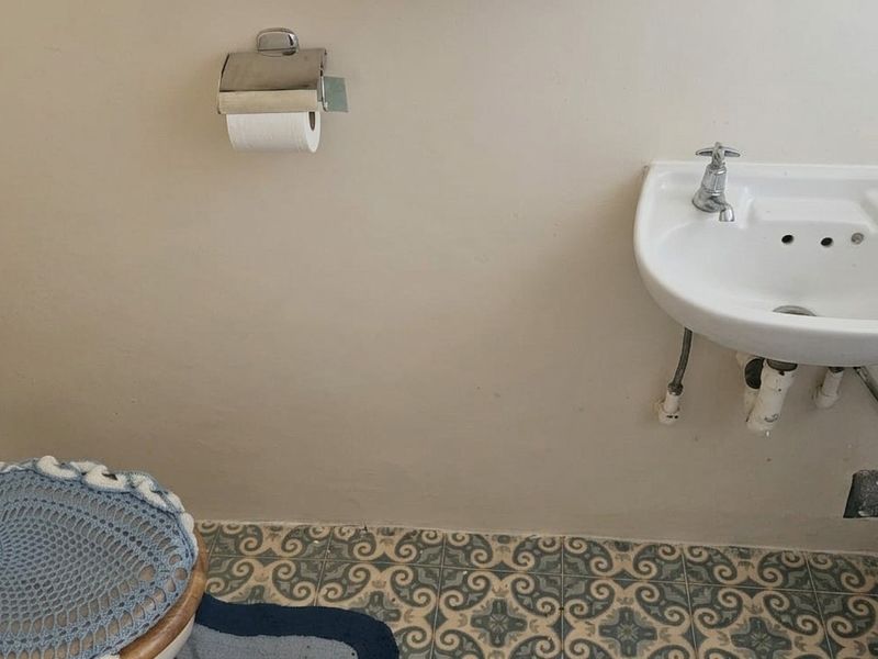 A compact bathroom featuring a wall-mounted basin, toilet, and patterned floor tiles, currently showing signs of wear and exposed plumbing.
