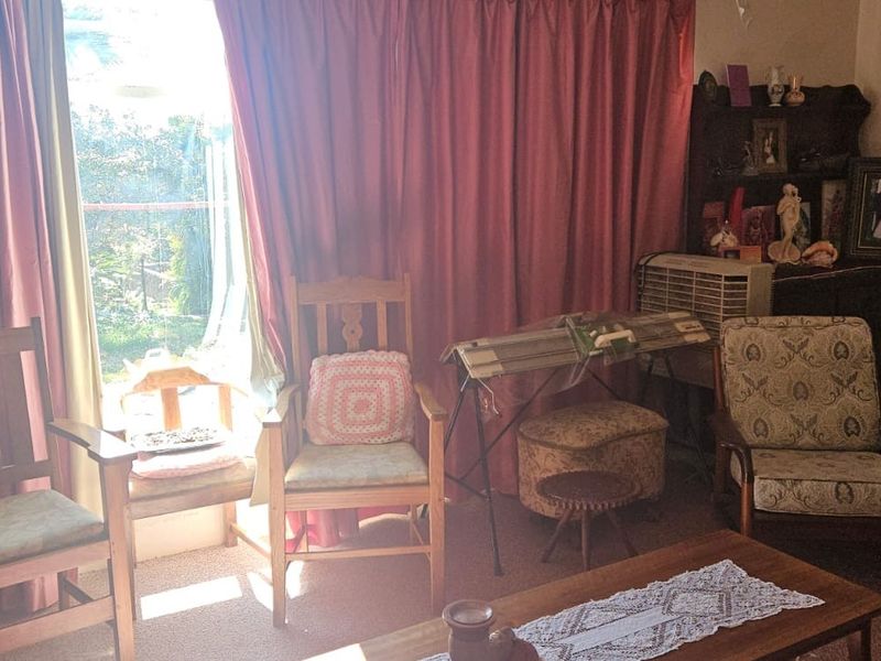 A living room area featuring large windows with curtains and carpeted flooring, offering a view to the exterior.
