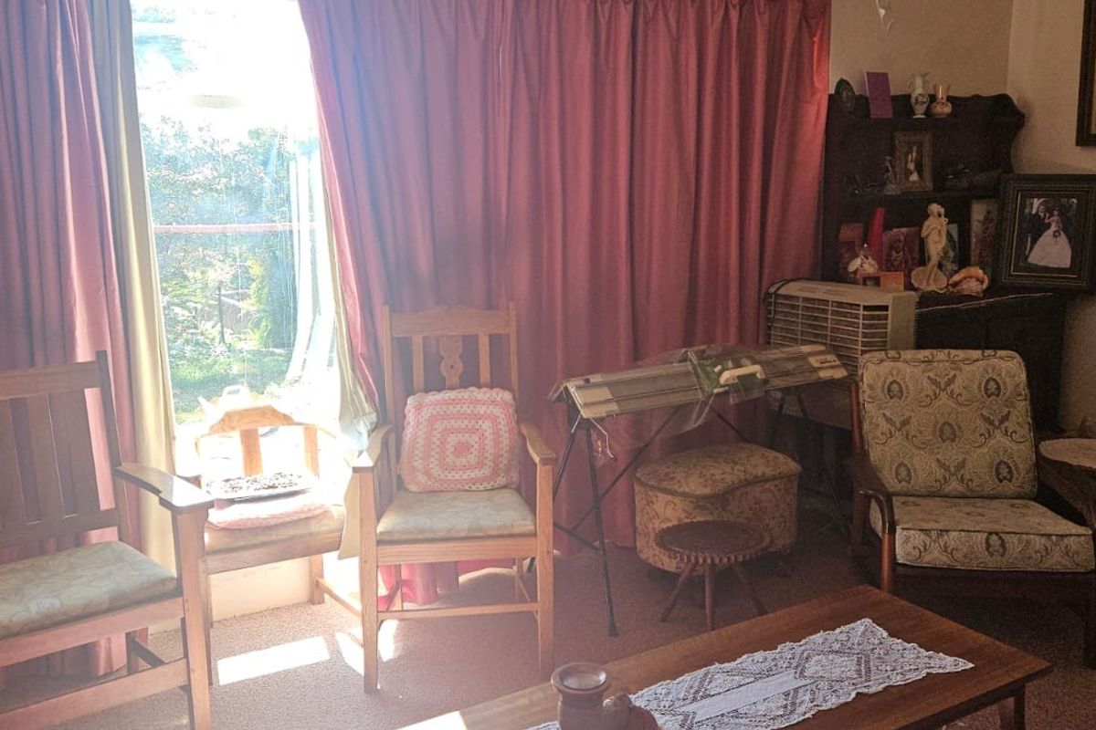 A living room area featuring large windows with curtains and carpeted flooring, offering a view to the exterior.