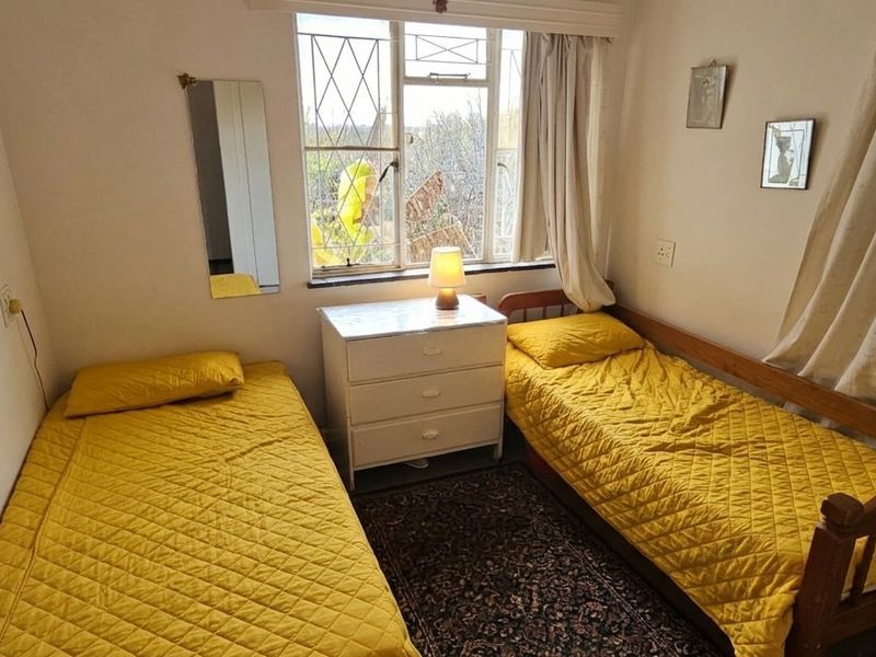 A functional bedroom featuring a steel-framed window with security bars and neutral wall finishes, suitable for a guest room or child's bedroom.