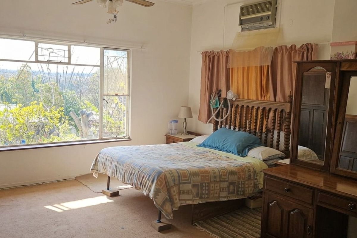 Spacious bedroom featuring large windows with natural light, carpeted flooring, and a wall-mounted air conditioning unit.
