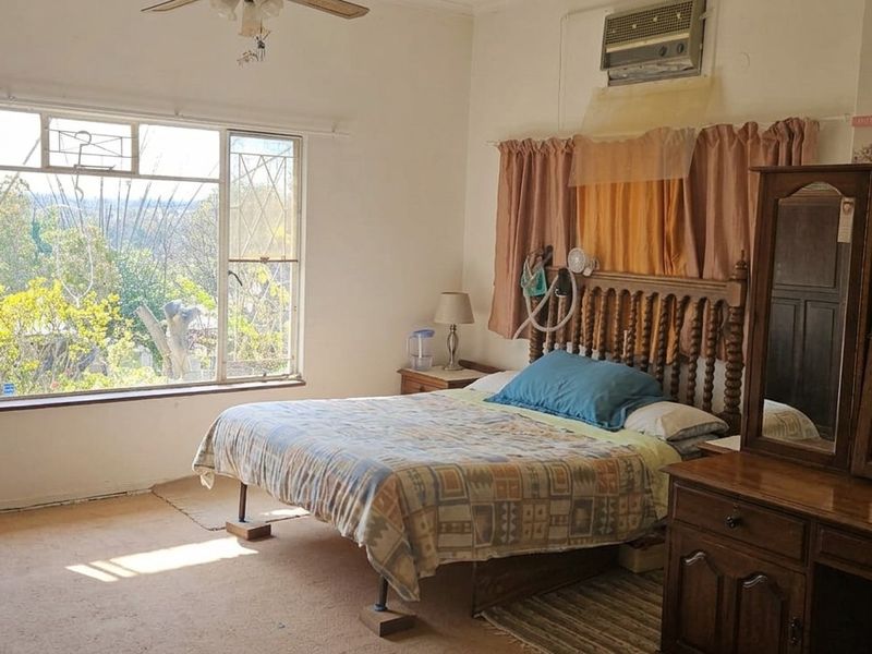 Spacious bedroom featuring large windows with natural light, carpeted flooring, and a wall-mounted air conditioning unit.