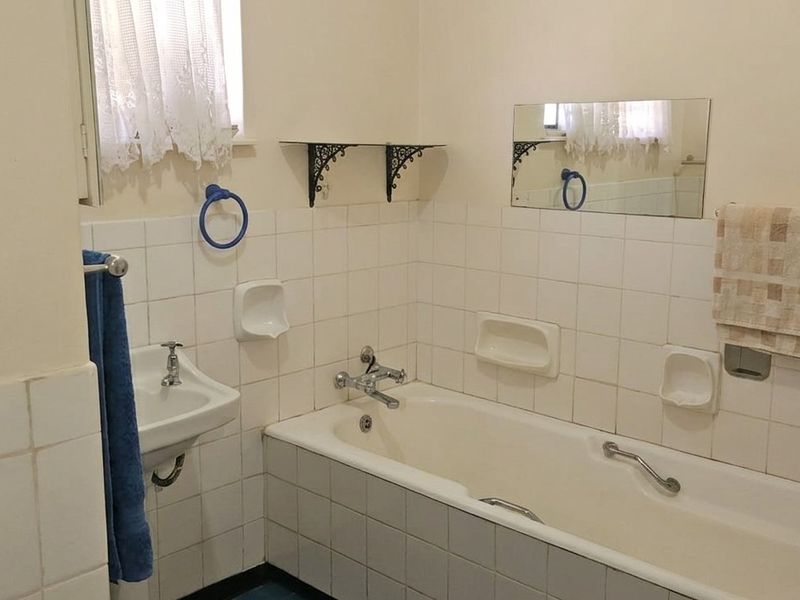 A dated bathroom featuring a standard bathtub, wall-mounted basin, and tiled wall finishes, offering potential for a modern renovation.