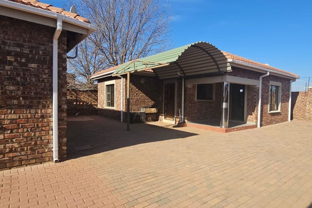 A spacious paved rear courtyard featuring face brick townhouse architecture, a protective metal awning, and secure perimeter walling.