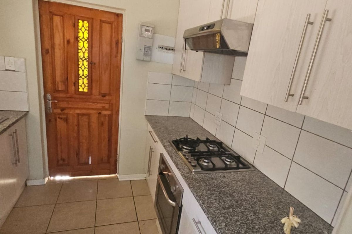 A functional kitchen featuring granite countertops, a gas hob, built-in oven, extractor fan, and tiled backsplash with direct access to an exterior timber door.