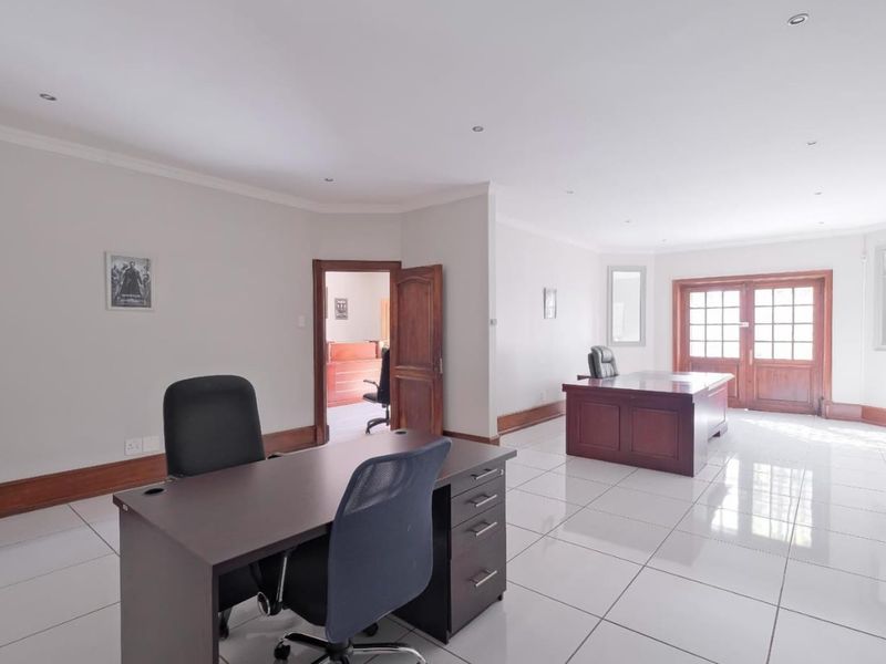 Spacious commercial office area featuring polished tiled flooring, recessed lighting, and wooden french doors leading to an exterior space.