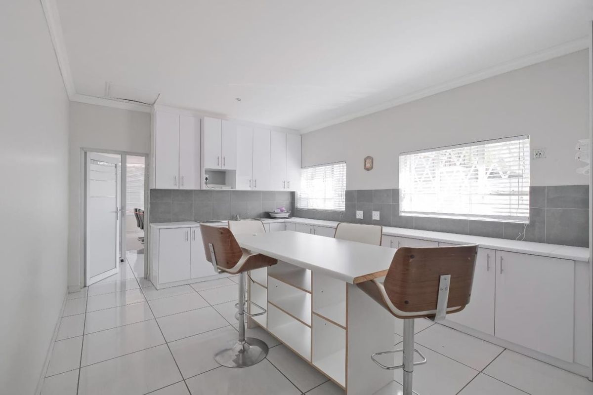 A bright, modern kitchen featuring white built-in cabinetry, a central island, tiled flooring, and a neutral tiled backsplash.