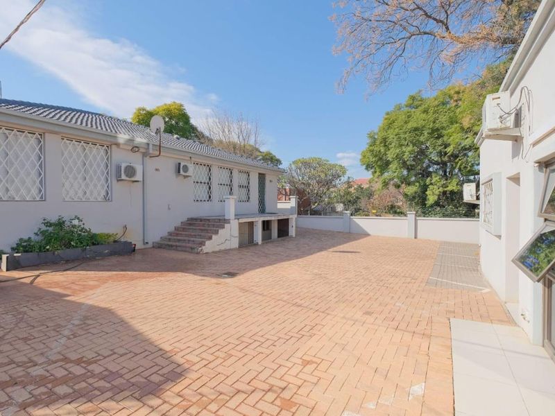 A spacious paved rear courtyard area featuring exterior security bars, mounted air conditioning units, and a surrounding boundary wall.
