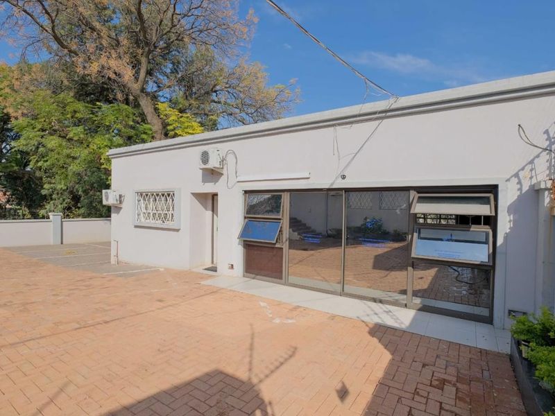 Rear exterior view of the commercial property featuring a paved courtyard, sliding glass doors, and perimeter security fencing.