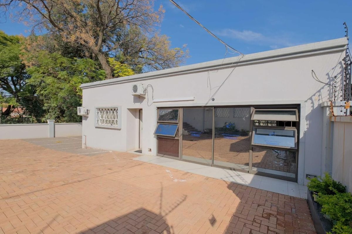 Rear exterior view of the commercial property featuring a paved courtyard, sliding glass doors, and perimeter security fencing.