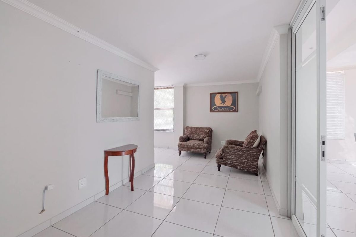 A bright, open-plan living area featuring polished white floor tiles, coved ceilings, and a sliding glass door providing natural light.