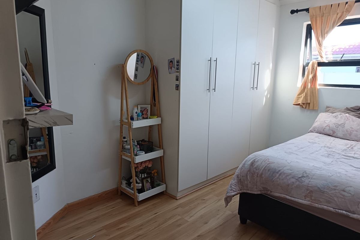 A well-lit bedroom featuring light-toned laminate flooring and floor-to-ceiling built-in cupboards, providing ample storage space.