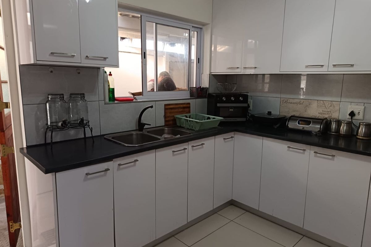 A functional kitchen featuring white gloss cabinetry, black countertops, a double bowl stainless steel sink, and tiled backsplash with neutral floor tiles.