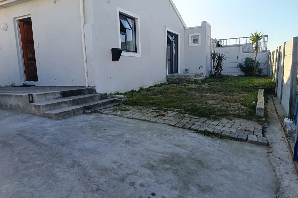 Rear exterior view of the property featuring a concrete driveway, paved walkway, and a fenced garden area with potential for landscaping improvements.