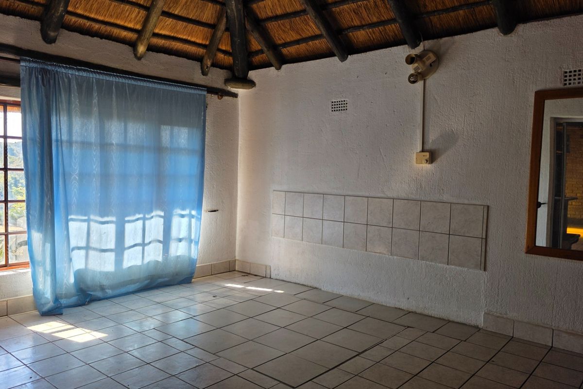 An empty living area featuring a traditional thatched roof with exposed timber rafters, ceramic tiled flooring, and a tiled wall accent.