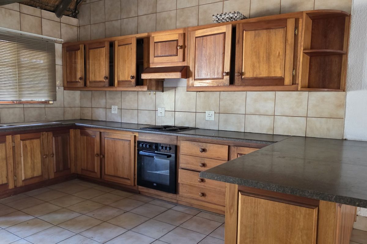 A functional kitchen featuring wooden cabinetry, built-in oven, hob, extractor fan, and tiled finishes, offering a classic farm-style aesthetic.