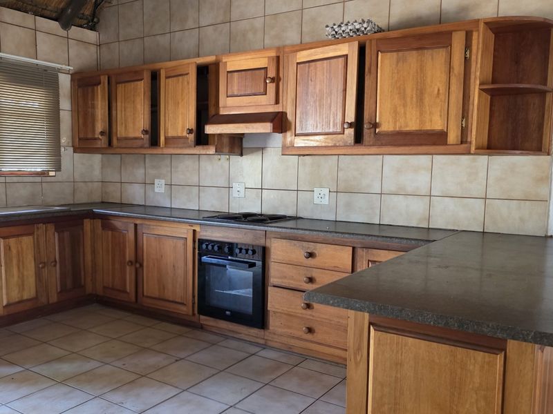 A functional kitchen featuring wooden cabinetry, built-in oven, hob, extractor fan, and tiled finishes, offering a classic farm-style aesthetic.