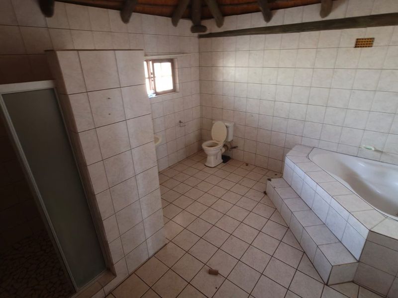 A spacious bathroom featuring a built-in bathtub, separate shower enclosure, and toilet, finished with tiled surfaces and a traditional thatched roof ceiling.