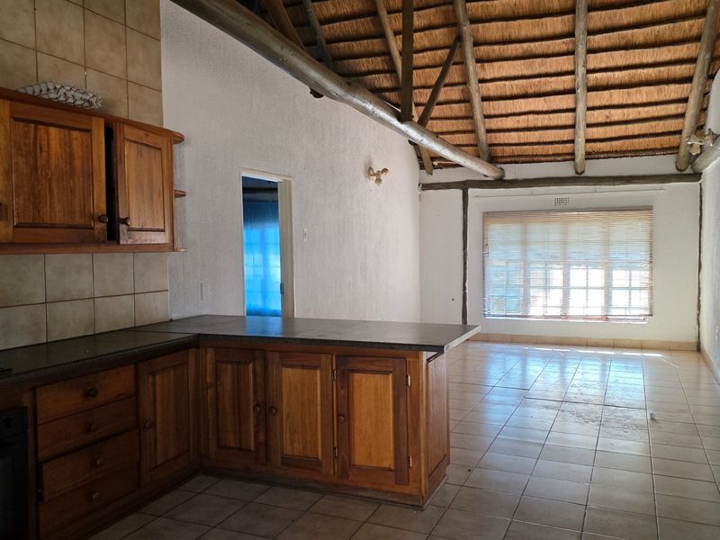 Open-plan kitchen and living area featuring a high thatched roof with exposed timber beams, tiled flooring, and wooden cabinetry.