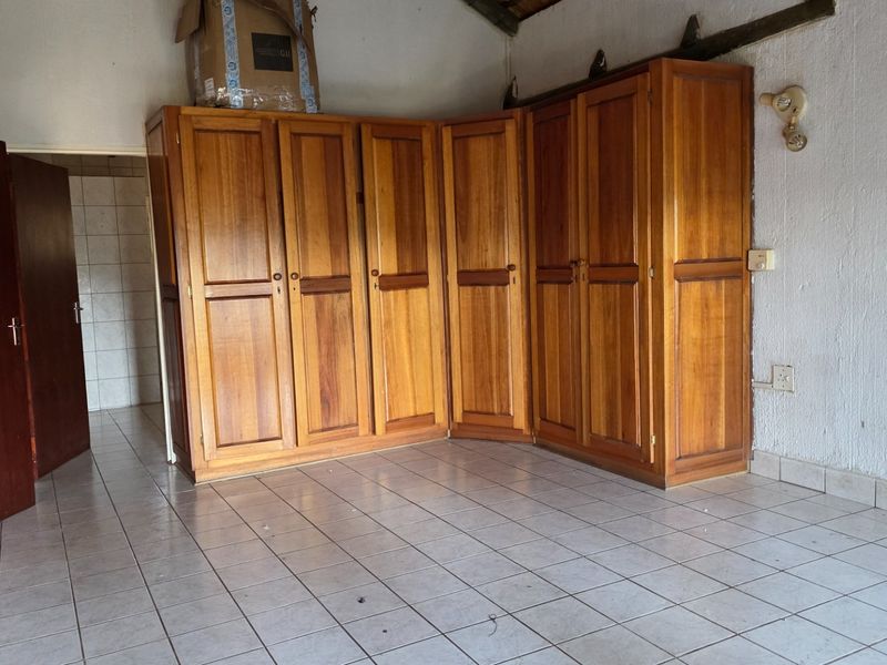 Bedroom featuring built-in wooden cupboards and tiled flooring, requiring cosmetic updates to the wall finishes.