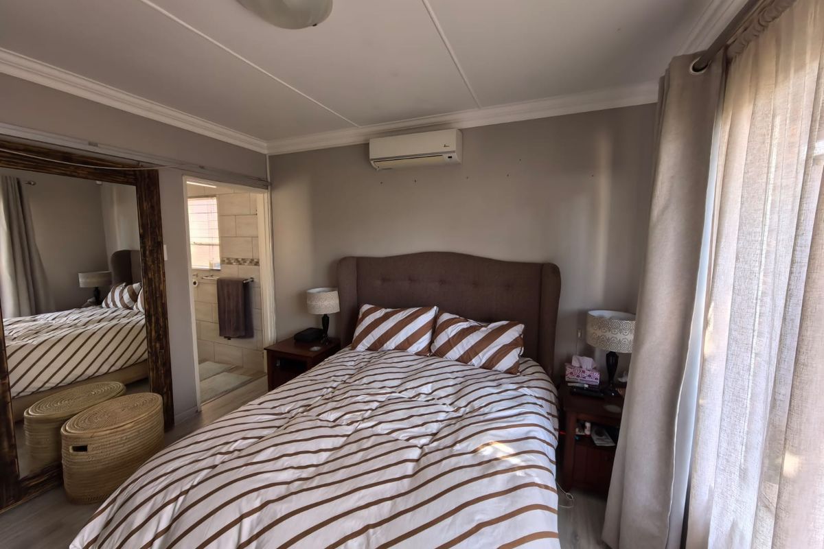 A bedroom featuring an en-suite bathroom, wall-mounted air conditioning unit, and neutral finishes, providing a functional and comfortable living space.