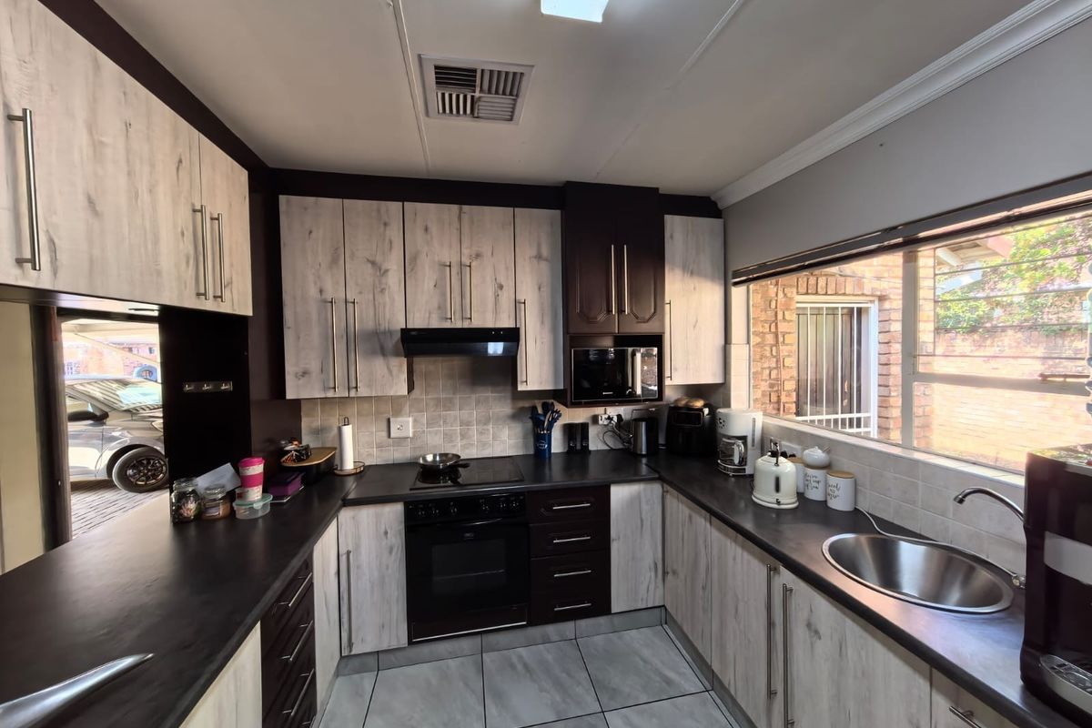 A functional kitchen featuring two-tone cabinetry, dark laminate countertops, built-in oven and hob, and a large window providing natural light.
