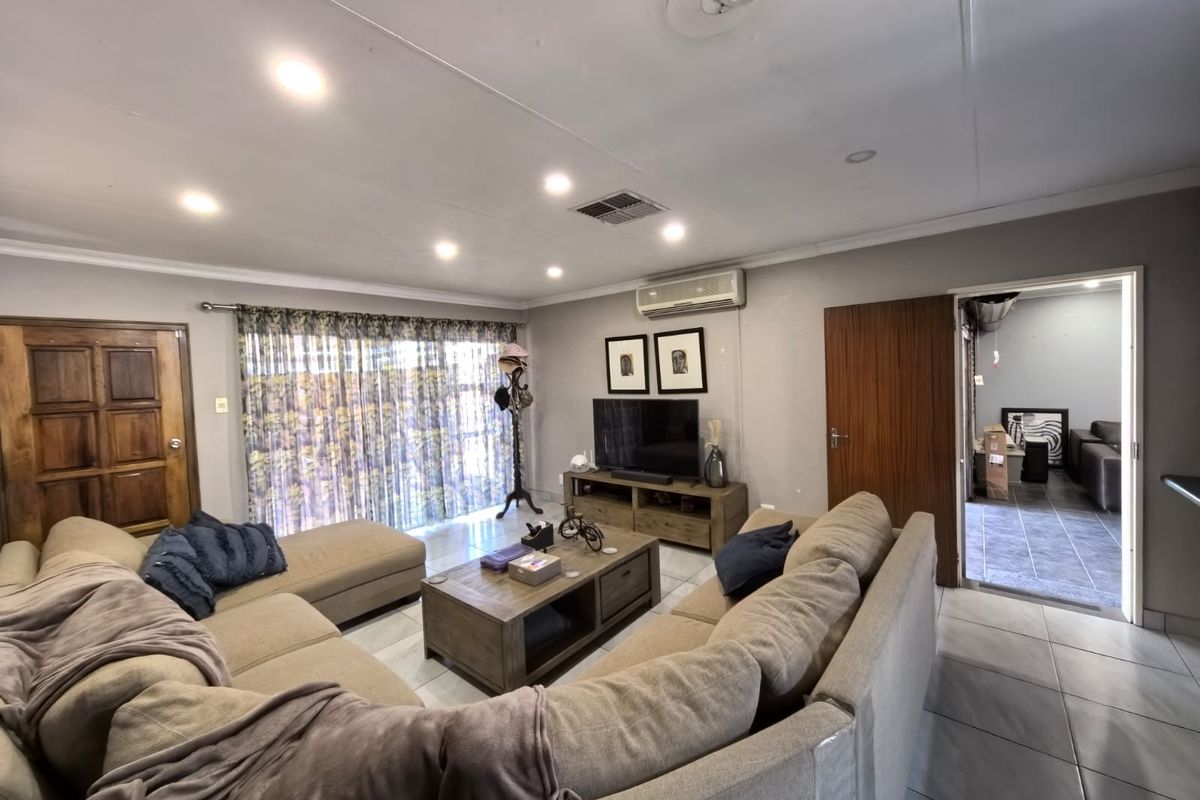 A spacious living room featuring tiled flooring, recessed downlighting, and a wall-mounted air conditioning unit, with direct access to an outdoor area.