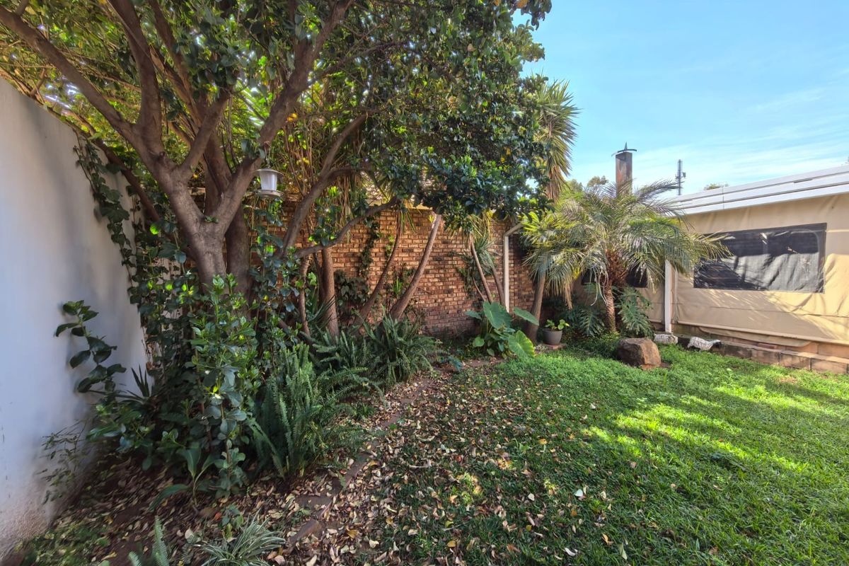 A private rear garden featuring a lawn, mature trees, and a brick boundary wall, adjacent to a covered patio area.