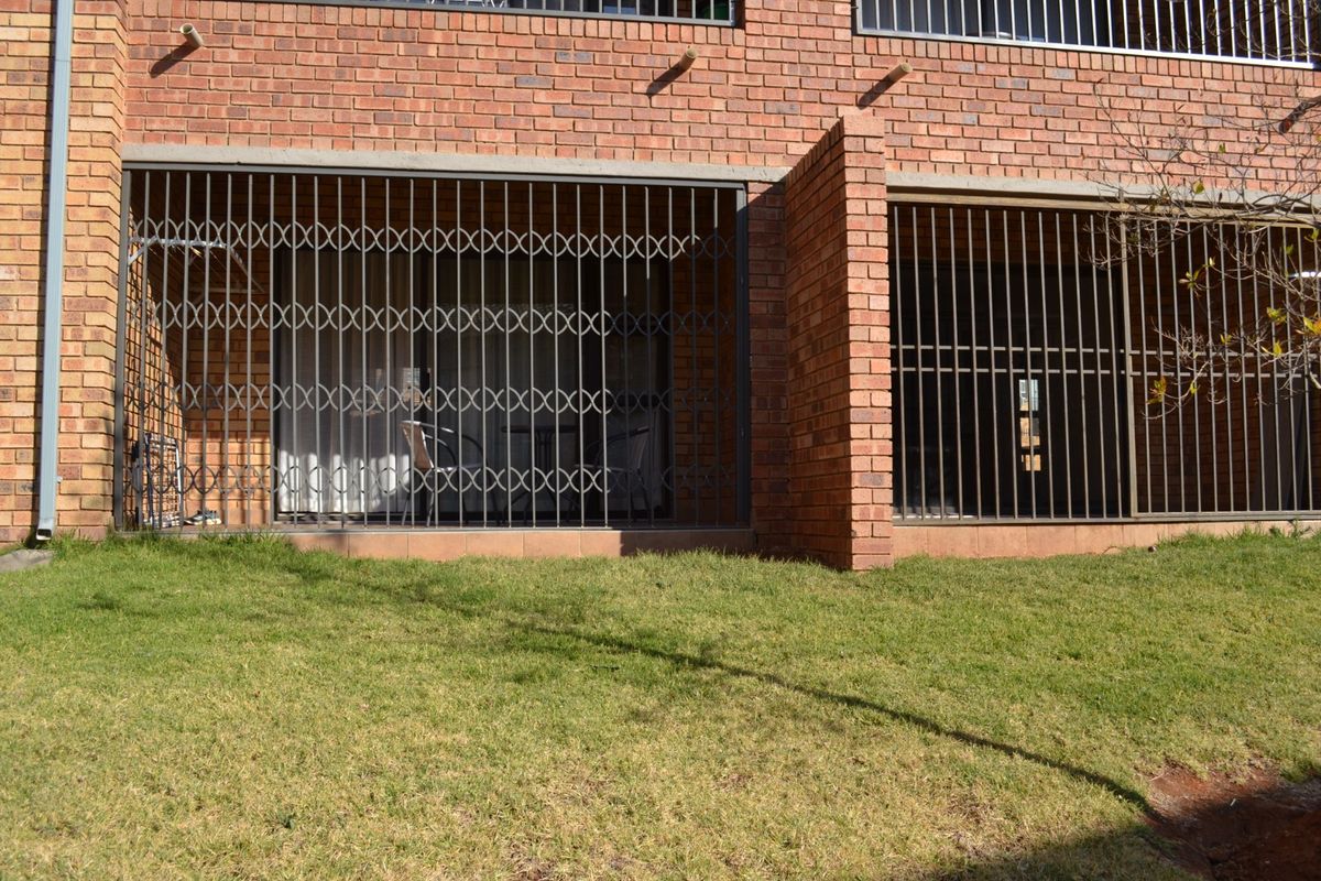 Rear exterior view of an apartment featuring a brick facade, tiled patio area, and heavy-duty security gates over the sliding glass doors.