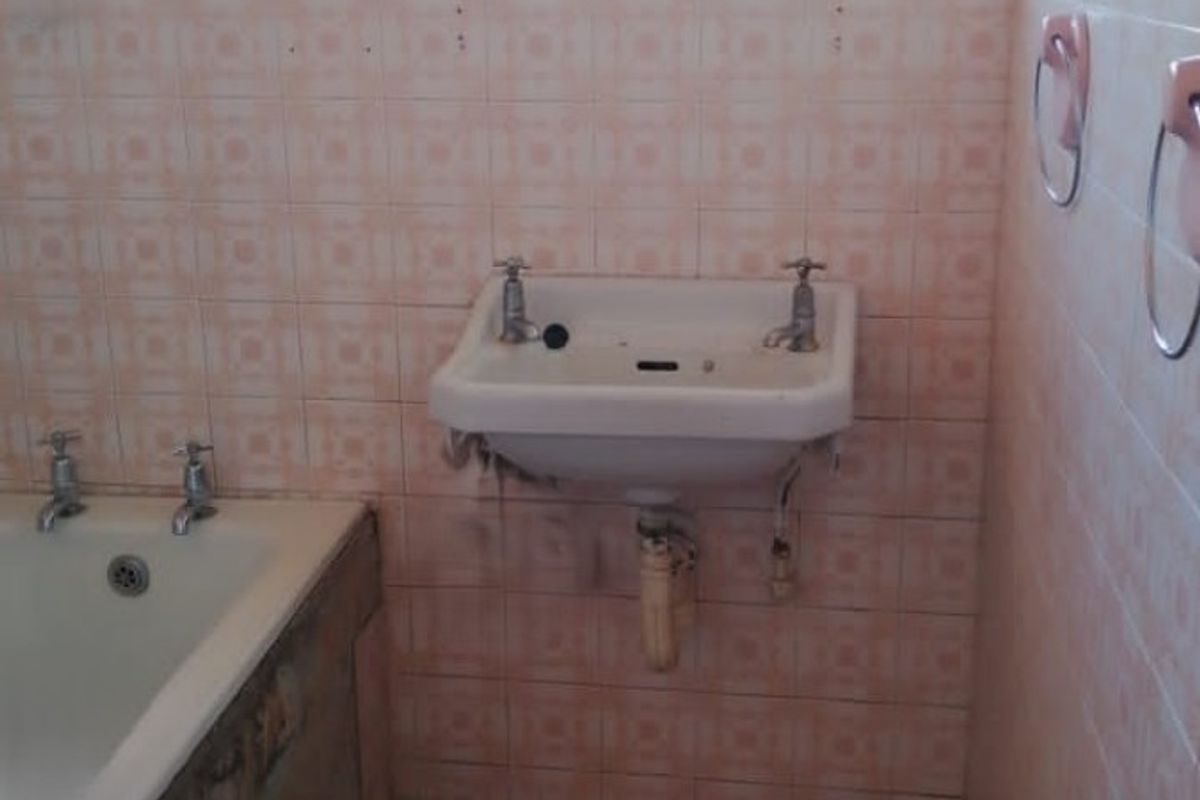 A dated bathroom featuring a wall-mounted basin, bathtub, and original tiled finishes, requiring renovation to modernize the space.