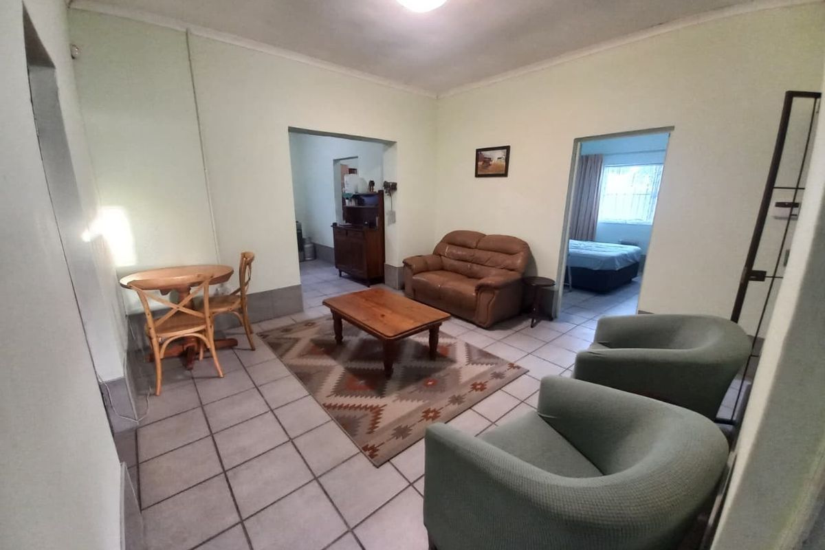 A functional living room area featuring neutral tiled flooring and coved ceilings, providing a central space with access to adjacent rooms.