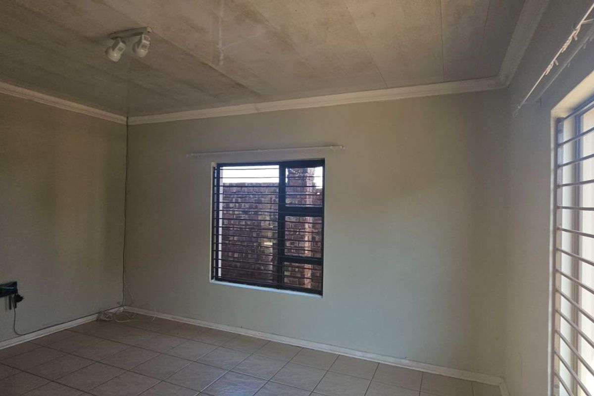 An empty living room featuring tiled flooring, security bars on the windows, and ceiling-mounted lighting, ready for a fresh update.