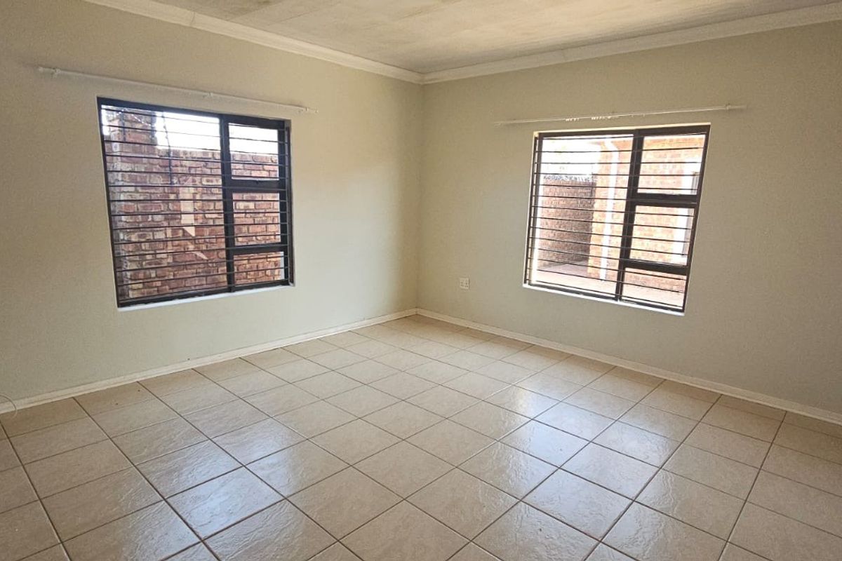 A bright, empty bedroom featuring neutral tiled flooring, cornicing, and windows fitted with security bars.
