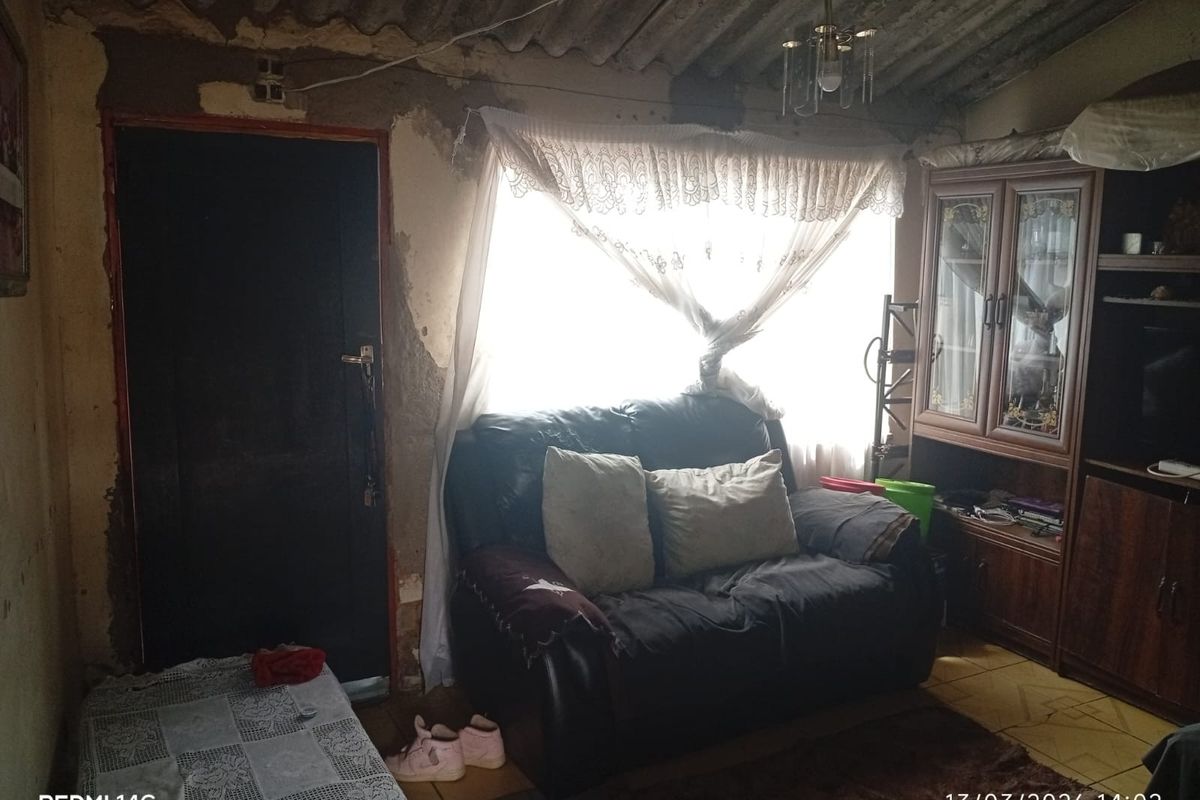 A living room space featuring tiled flooring and an exposed corrugated ceiling, currently requiring significant wall repairs and cosmetic renovation.