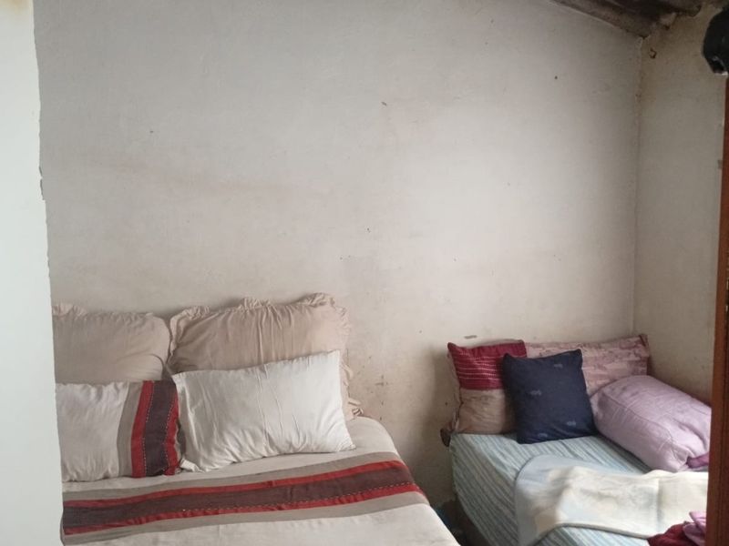 A compact bedroom featuring exposed roof rafters and corrugated sheeting, requiring cosmetic updates to the wall finishes and overall interior presentation.