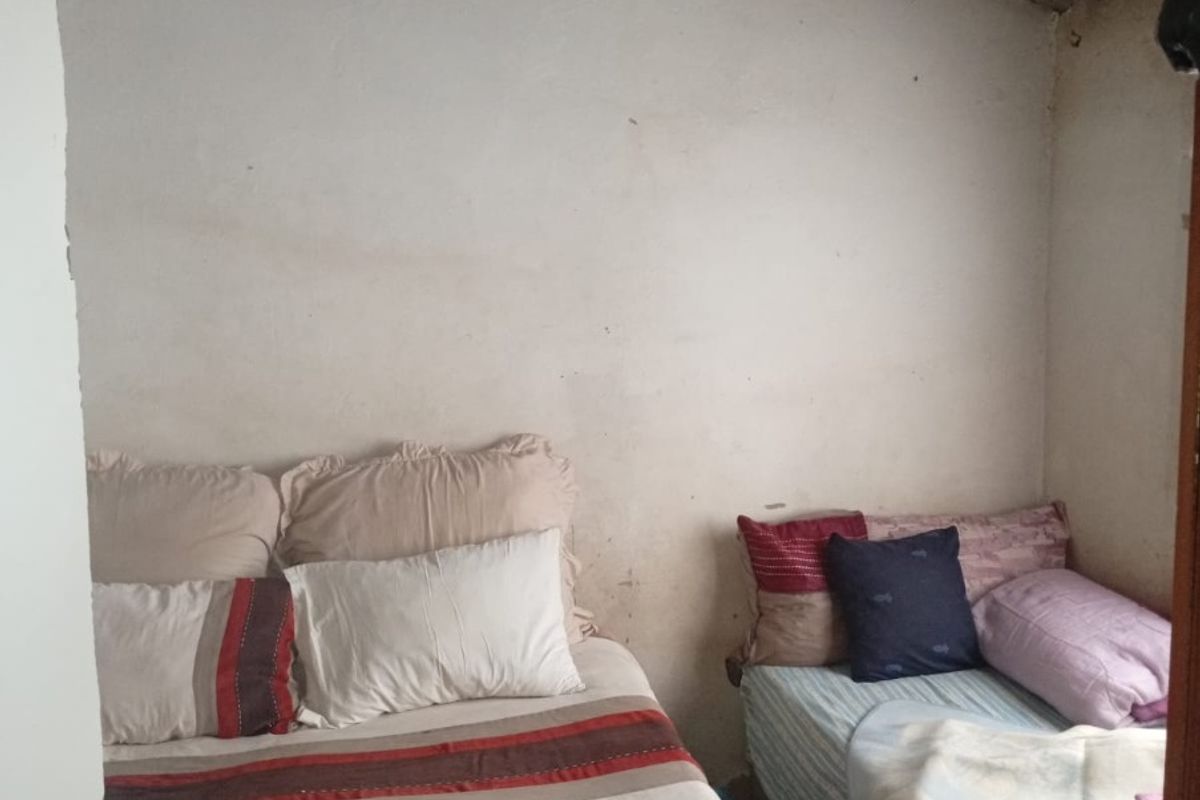 A compact bedroom featuring exposed roof rafters and corrugated sheeting, requiring cosmetic updates to the wall finishes and overall interior presentation.