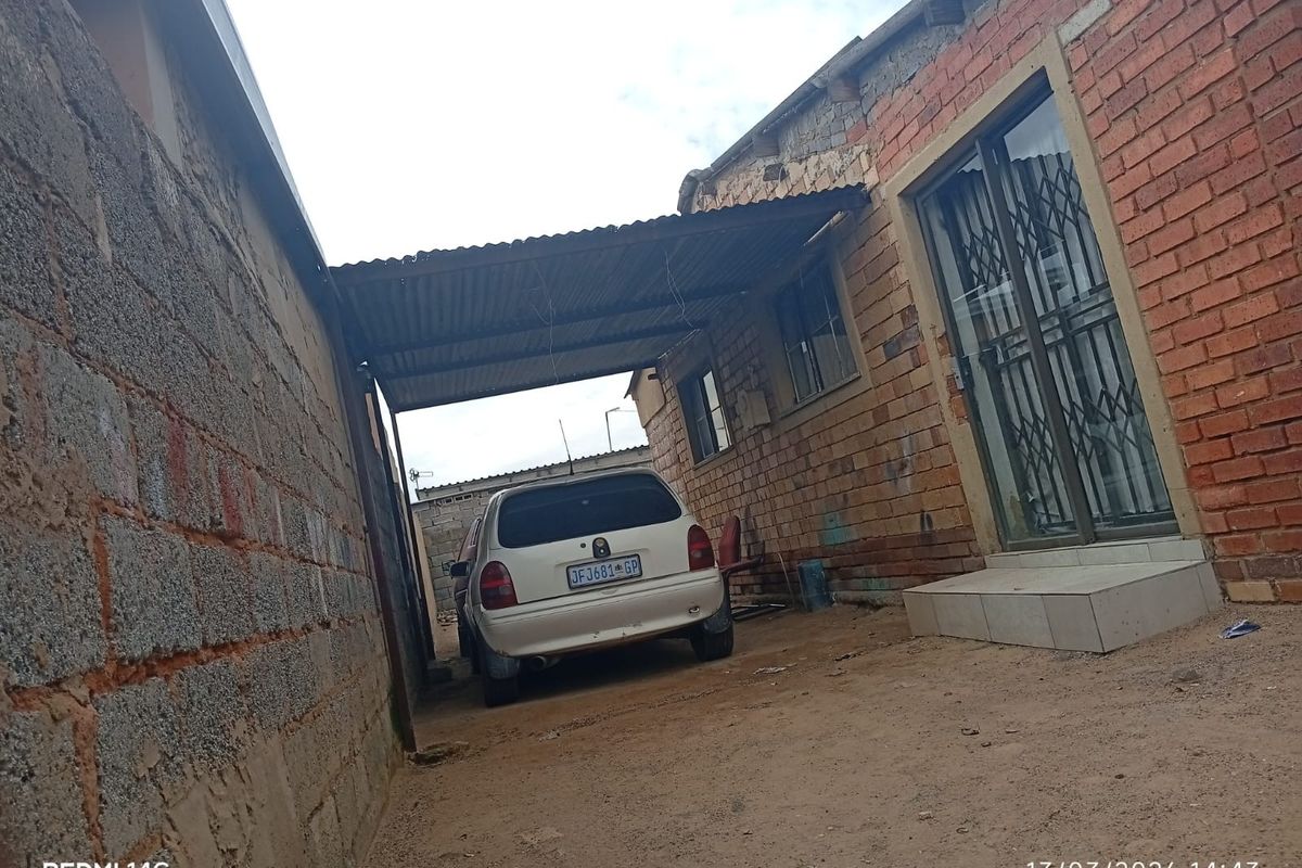 Rear exterior view of the property featuring exposed brick walls, a corrugated iron roof structure, and a sliding door with a security gate.