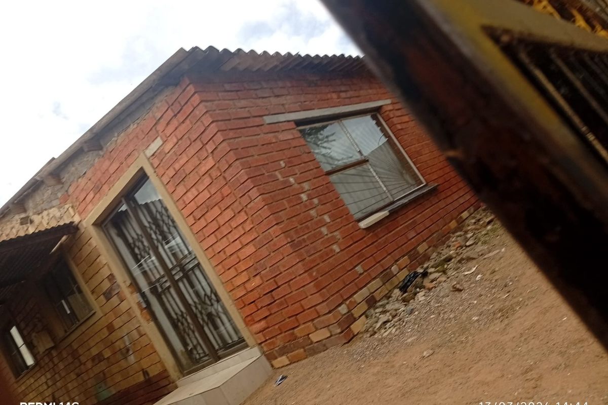 Exterior view of a single-story house featuring exposed brick walls, a corrugated roof, and security-fitted doors and windows.