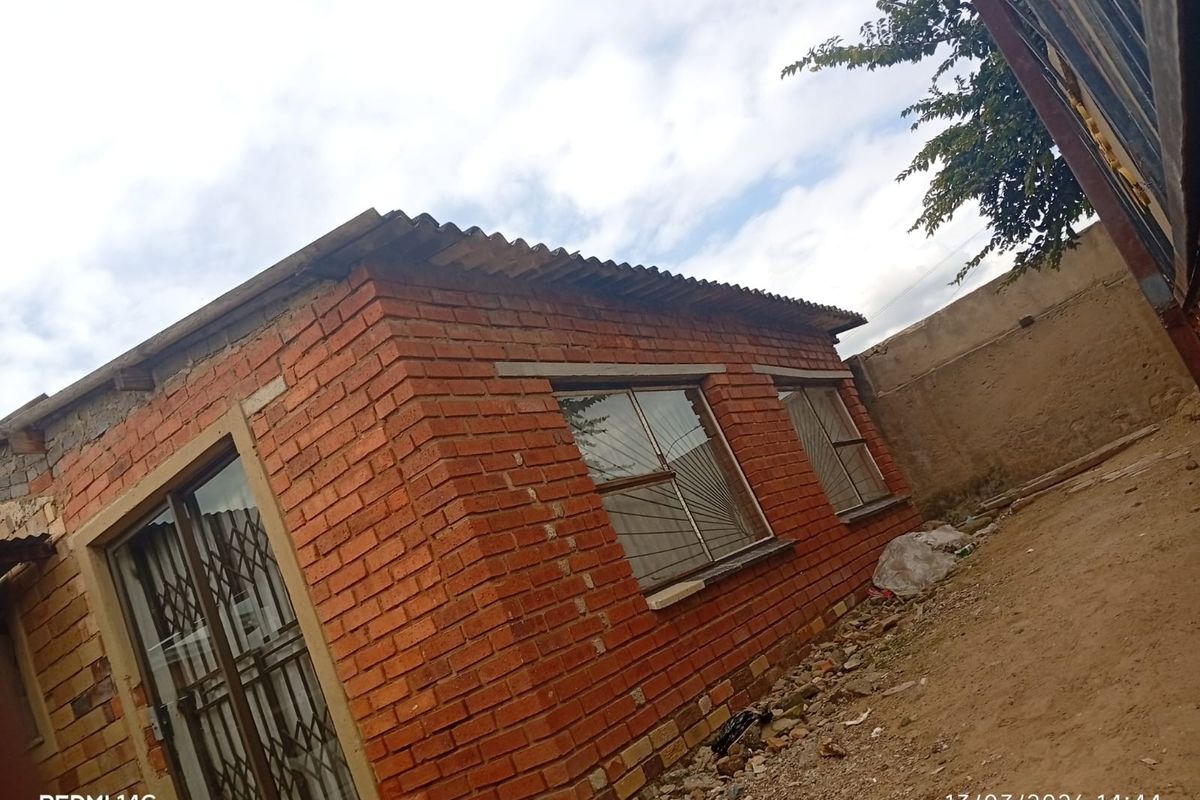 Exterior view of a brick structure featuring metal security gates and window bars, set against an unpaved outdoor area.