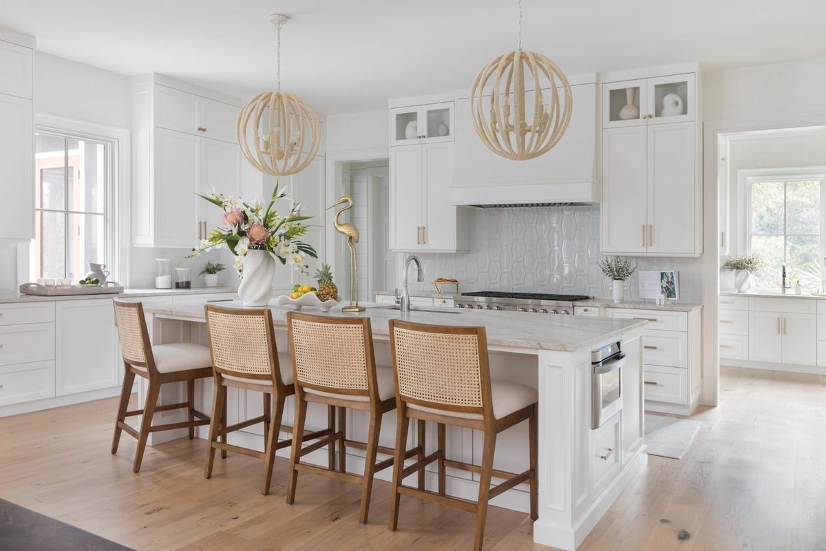 A bright, modern kitchen featuring white shaker cabinetry, a large central island with stone countertops, high-end appliances, and elegant pendant lighting.