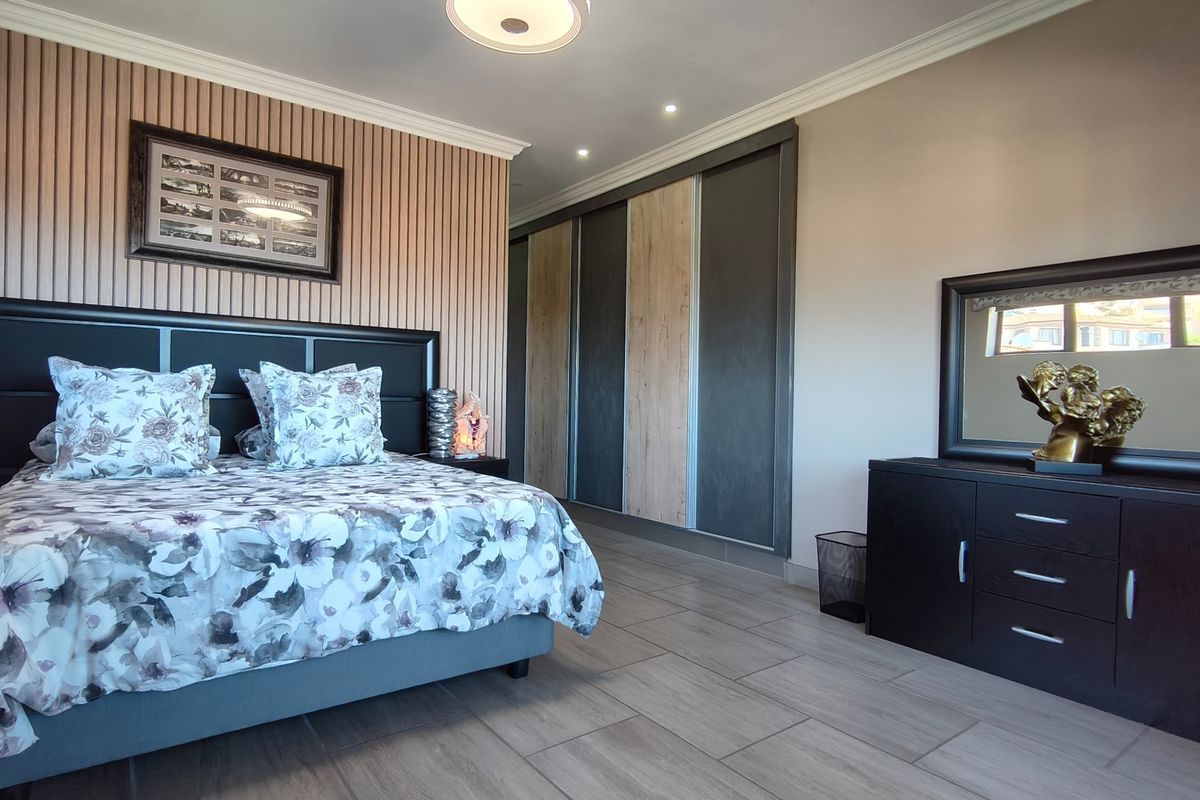 A well-maintained bedroom featuring modern built-in sliding wardrobes, stylish slatted timber wall paneling, and neutral tiled flooring.
