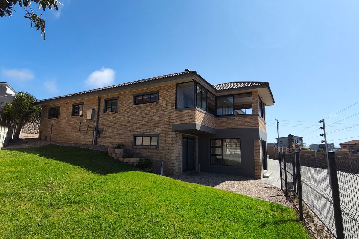 Rear view of a double-story brick house featuring modern aluminum window frames, a well-maintained lawn, and secure perimeter electric fencing.