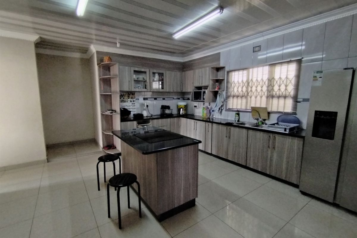 Spacious kitchen featuring wood-finish cabinetry, granite countertops, a central island, and tiled flooring with ample storage and workspace.